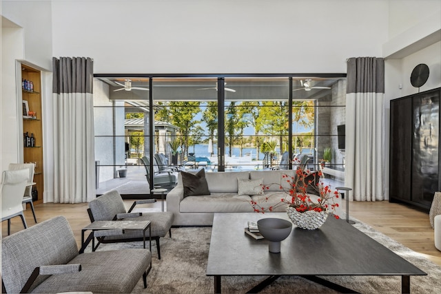 living room with ceiling fan, floor to ceiling windows, a sunroom, a towering ceiling, and wood finished floors