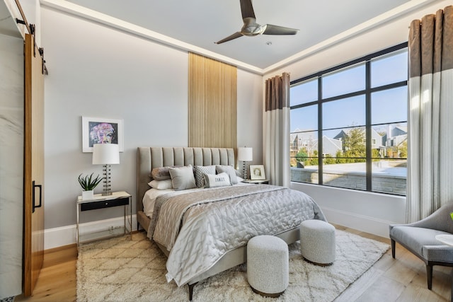 bedroom with light wood-style floors, a ceiling fan, a barn door, and baseboards