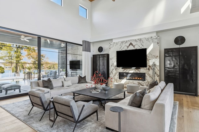 living area featuring wood finished floors, a ceiling fan, a fireplace, and a towering ceiling