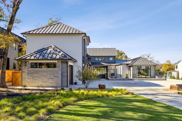 view of front facade featuring stucco siding, a standing seam roof, metal roof, stone siding, and a front yard