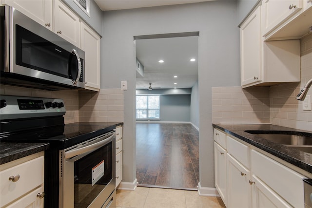 kitchen with dark stone countertops, white cabinetry, a sink, stainless steel appliances, and recessed lighting