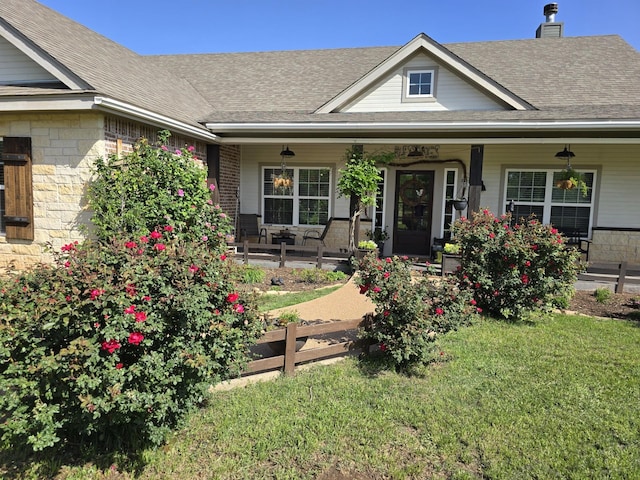 view of front of house with a porch, a chimney, roof with shingles, and a front lawn
