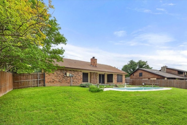 rear view of property with a tile roof, a lawn, a fenced backyard, and a chimney