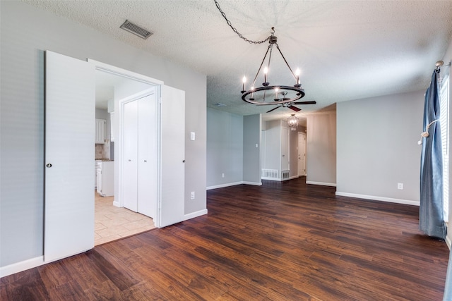 interior space with a textured ceiling, visible vents, a chandelier, baseboards, and wood finished floors