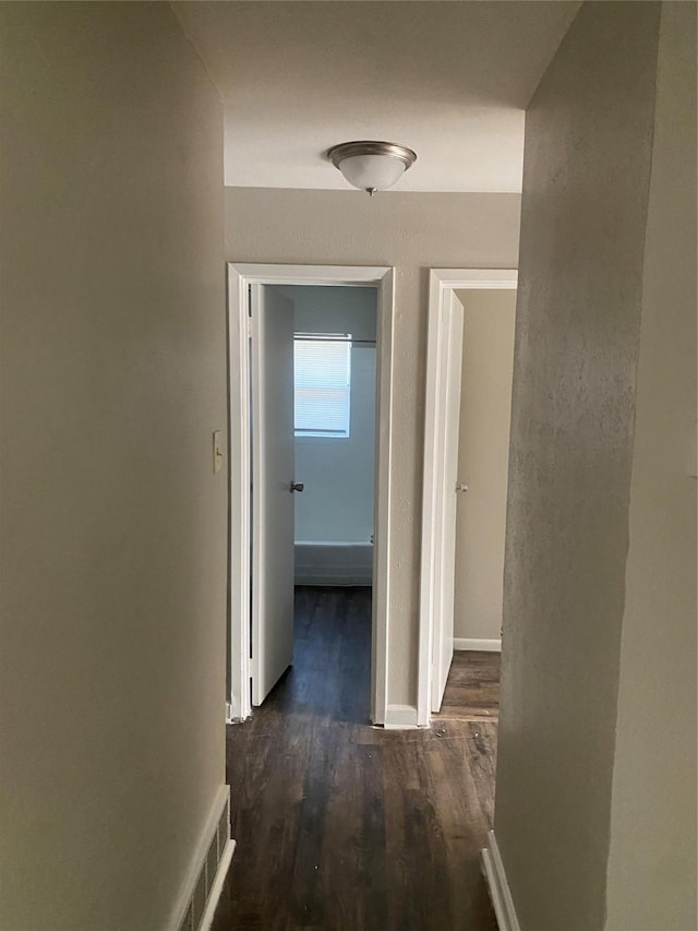hallway featuring visible vents, dark wood finished floors, and baseboards