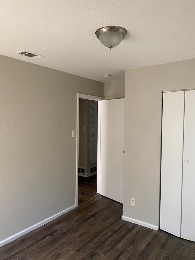 unfurnished bedroom with a closet, dark wood-style flooring, visible vents, and baseboards