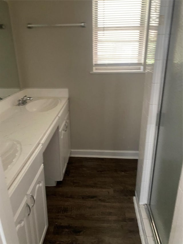 bathroom featuring a sink, a stall shower, double vanity, baseboards, and wood finished floors