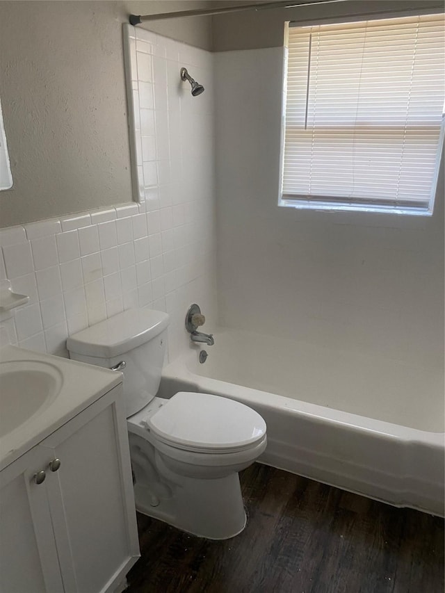 full bath with washtub / shower combination, toilet, tile walls, wood finished floors, and vanity