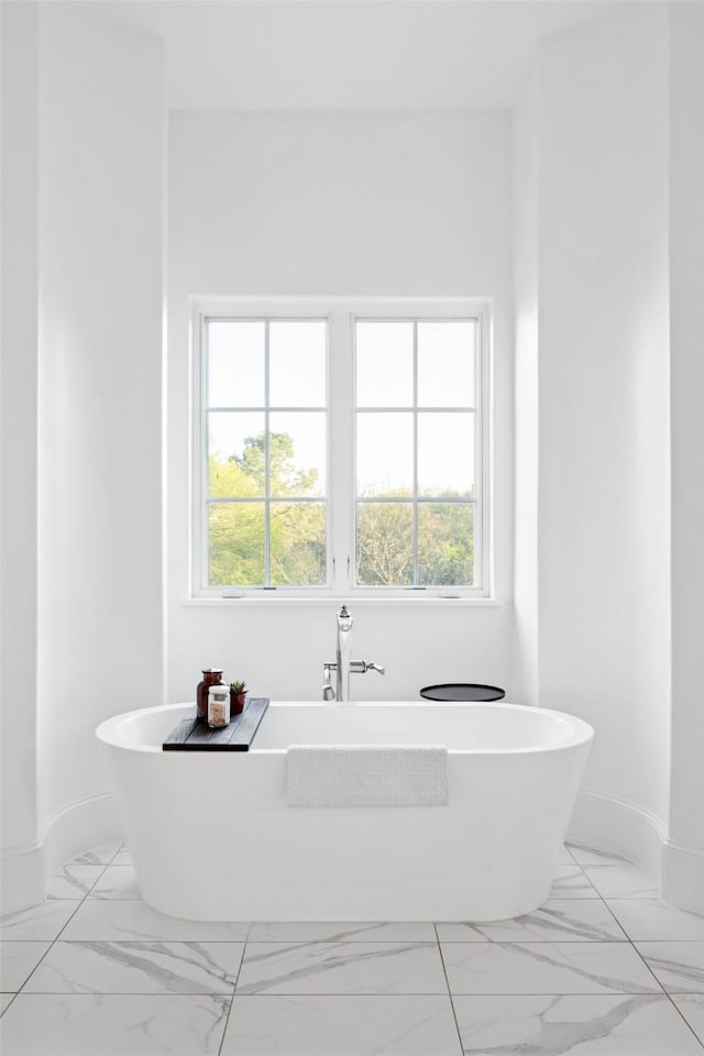 bathroom featuring a freestanding tub, plenty of natural light, marble finish floor, and baseboards