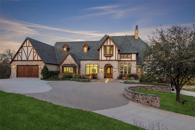 english style home with a chimney, stucco siding, a yard, curved driveway, and stone siding