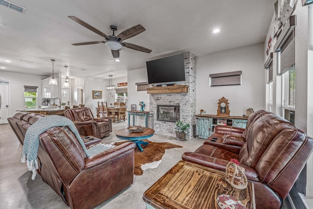 living area featuring a fireplace, visible vents, ceiling fan, and plenty of natural light