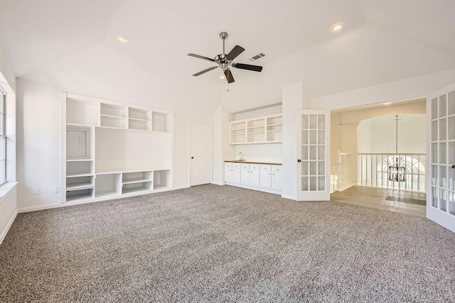 unfurnished living room with visible vents, ceiling fan with notable chandelier, carpet flooring, baseboards, and high vaulted ceiling