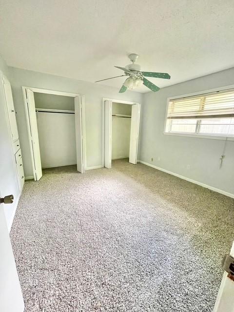 unfurnished bedroom featuring two closets, a ceiling fan, and baseboards