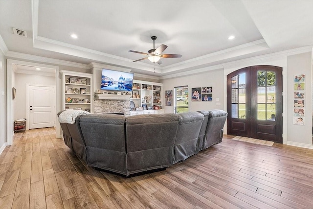 living room featuring visible vents, a tray ceiling, light wood-type flooring, french doors, and a ceiling fan