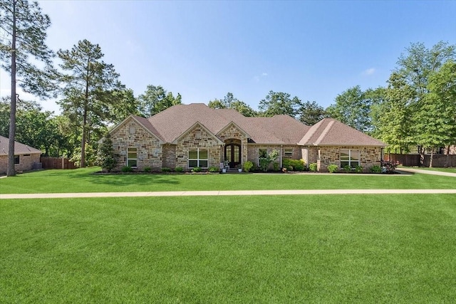 view of front of house featuring a front lawn, stone siding, and fence