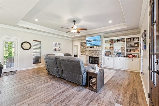 living area with crown molding, a tray ceiling, light wood-type flooring, a fireplace, and a ceiling fan