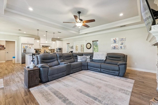 living room with visible vents, ceiling fan, a tray ceiling, baseboards, and light wood finished floors