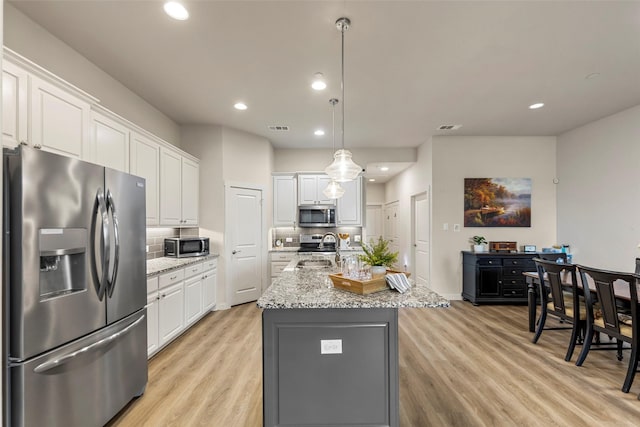 kitchen with tasteful backsplash, an island with sink, light wood-style flooring, stainless steel appliances, and white cabinetry