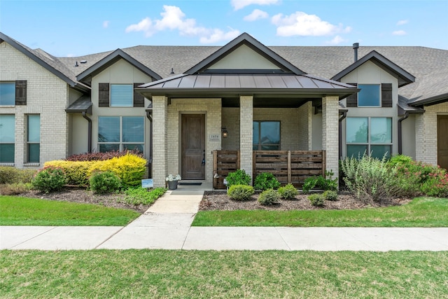view of front of house featuring a porch, brick siding, a standing seam roof, roof with shingles, and a front lawn