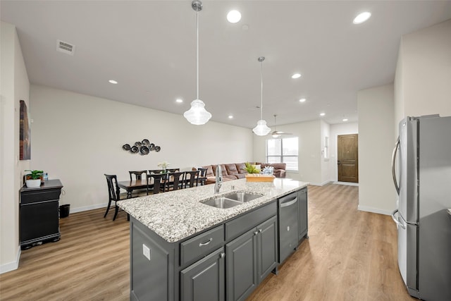 kitchen with a sink, stainless steel appliances, light wood-style floors, visible vents, and an island with sink