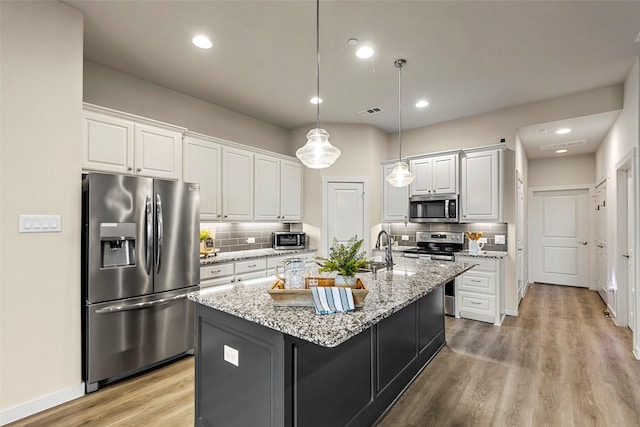 kitchen with tasteful backsplash, an island with sink, light wood-style floors, appliances with stainless steel finishes, and white cabinets
