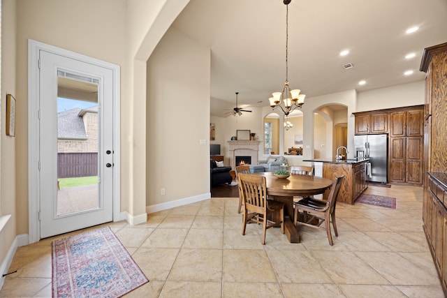 dining space featuring a warm lit fireplace, visible vents, baseboards, arched walkways, and ceiling fan with notable chandelier