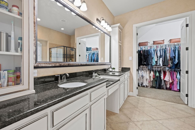 full bath with a spacious closet, a shower stall, double vanity, and a sink
