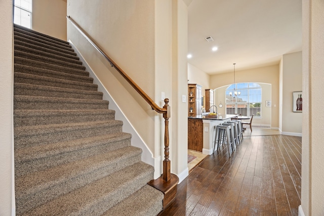 stairway with an inviting chandelier, visible vents, baseboards, arched walkways, and hardwood / wood-style floors