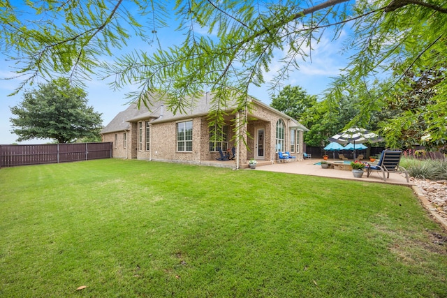 back of house featuring a patio, brick siding, a fenced backyard, and a lawn