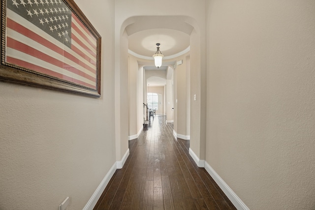 corridor with dark wood-style flooring, baseboards, and arched walkways