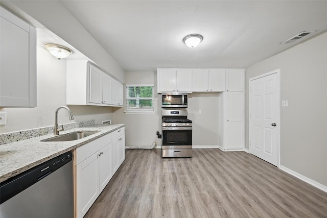 kitchen with light stone counters, a sink, appliances with stainless steel finishes, visible vents, and light wood finished floors