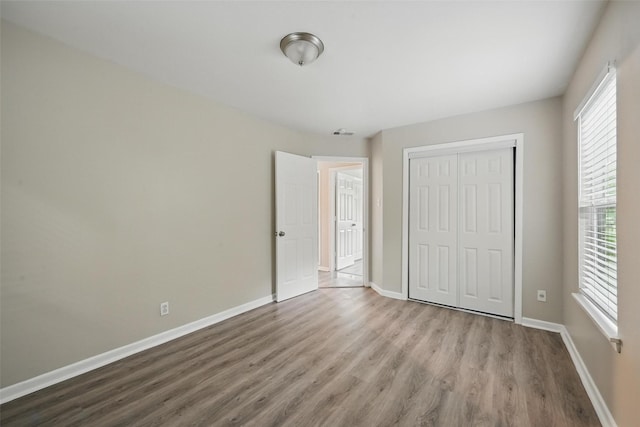 unfurnished bedroom with wood finished floors, a closet, baseboards, and multiple windows