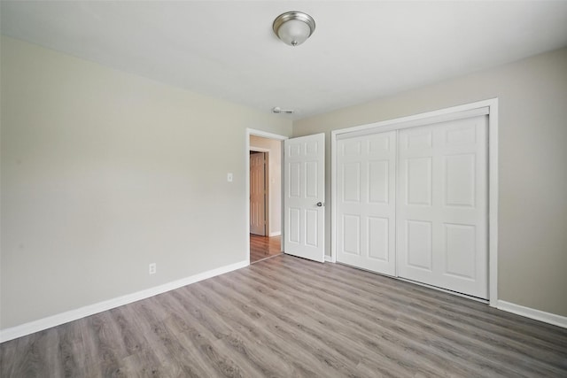 unfurnished bedroom featuring wood finished floors, a closet, and baseboards