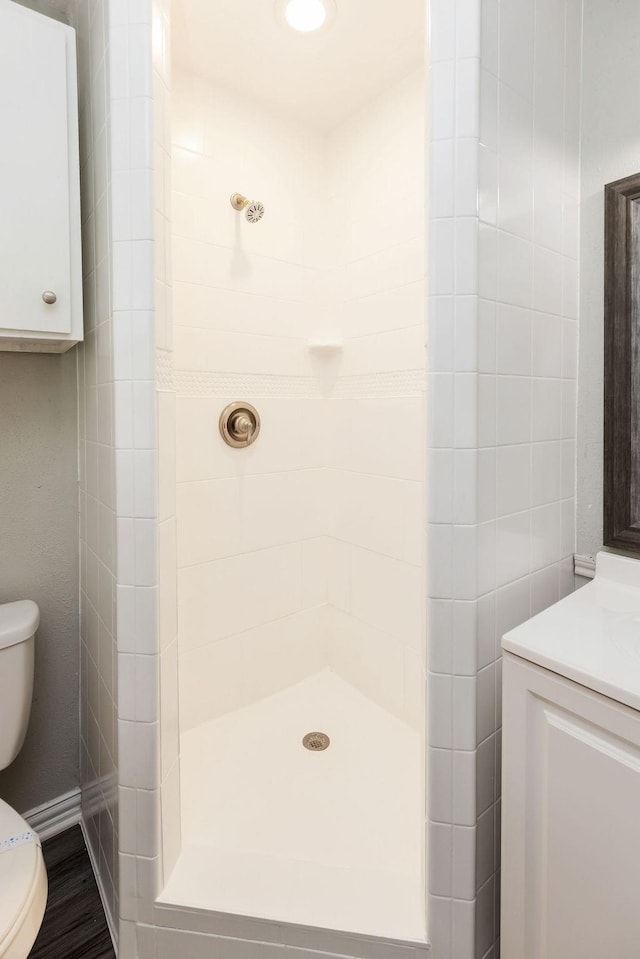 bathroom with toilet, tiled shower, and vanity