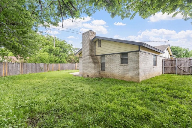 view of side of property featuring brick siding, a yard, a fenced backyard, and a chimney
