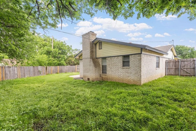 back of property featuring a chimney, a yard, brick siding, and a fenced backyard