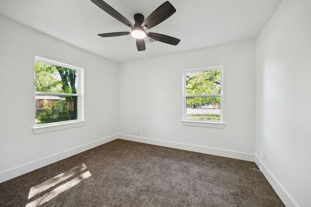 unfurnished room with ceiling fan, dark colored carpet, and plenty of natural light