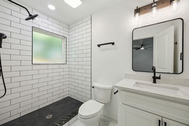 bathroom featuring a tile shower, toilet, a ceiling fan, and vanity