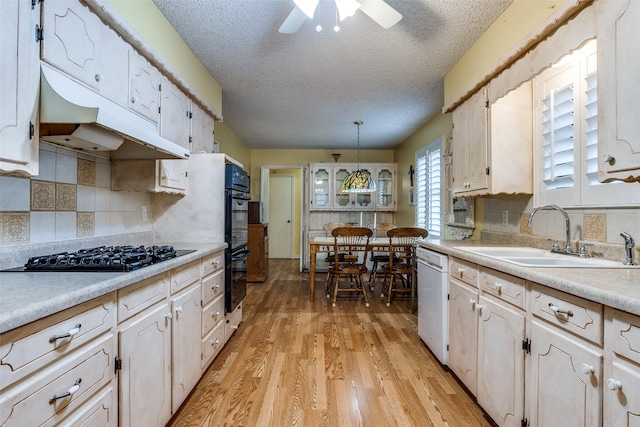 kitchen with under cabinet range hood, light countertops, black appliances, light wood finished floors, and a sink