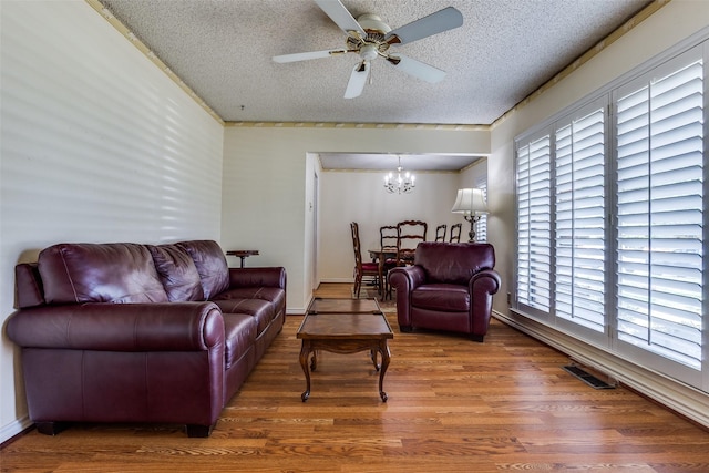 living area with visible vents, wood finished floors, ceiling fan with notable chandelier, and a textured ceiling