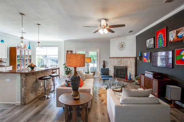 living area with a fireplace, wood finished floors, ceiling fan, and ornamental molding