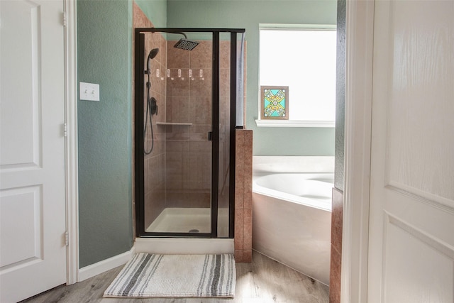 full bathroom featuring a stall shower, a textured wall, a bathtub, and wood finished floors