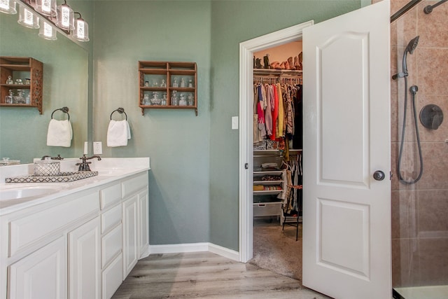 full bath featuring a tile shower, a sink, double vanity, wood finished floors, and a walk in closet