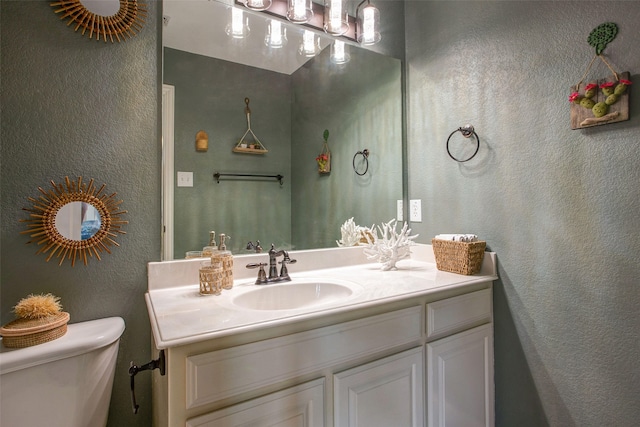 half bath with toilet, a textured wall, and vanity