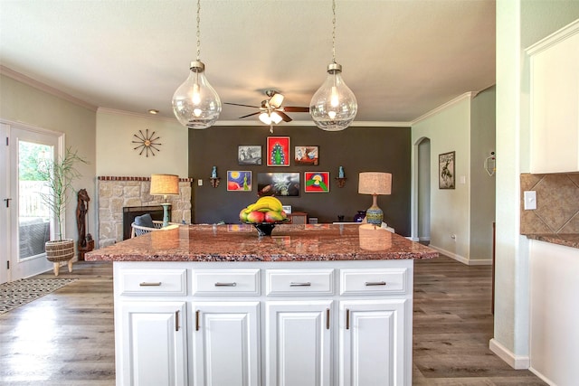 kitchen featuring wood finished floors, a ceiling fan, a stone fireplace, ornamental molding, and open floor plan
