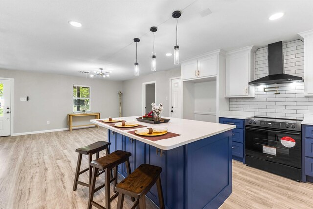 kitchen featuring blue cabinetry, wall chimney exhaust hood, light countertops, white cabinets, and black range with electric cooktop