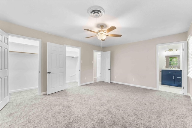 unfurnished bedroom featuring a walk in closet, ensuite bath, light carpet, and baseboards
