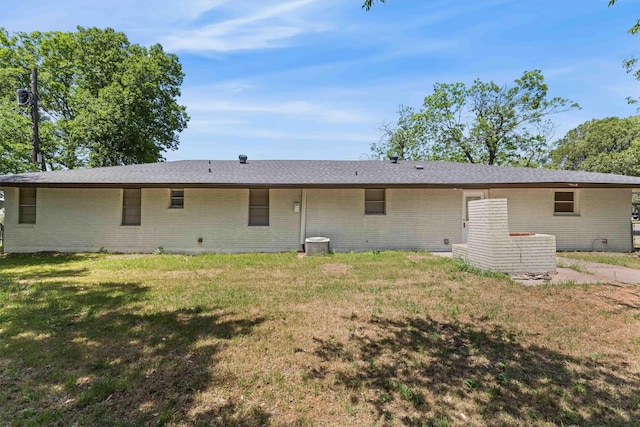 rear view of property featuring a lawn, cooling unit, a shingled roof, and brick siding