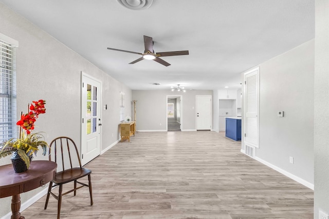 living area featuring ceiling fan, light wood-type flooring, a healthy amount of sunlight, and baseboards