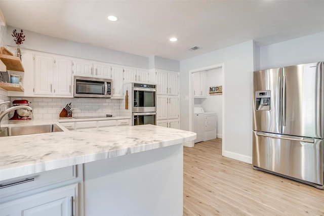 kitchen featuring decorative backsplash, stainless steel appliances, washing machine and clothes dryer, a sink, and visible vents